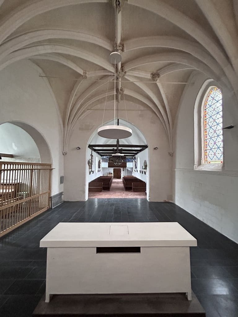 Intérieur d'une église avec un autel blanc au premier plan, un plafond voûté et un vitrail.