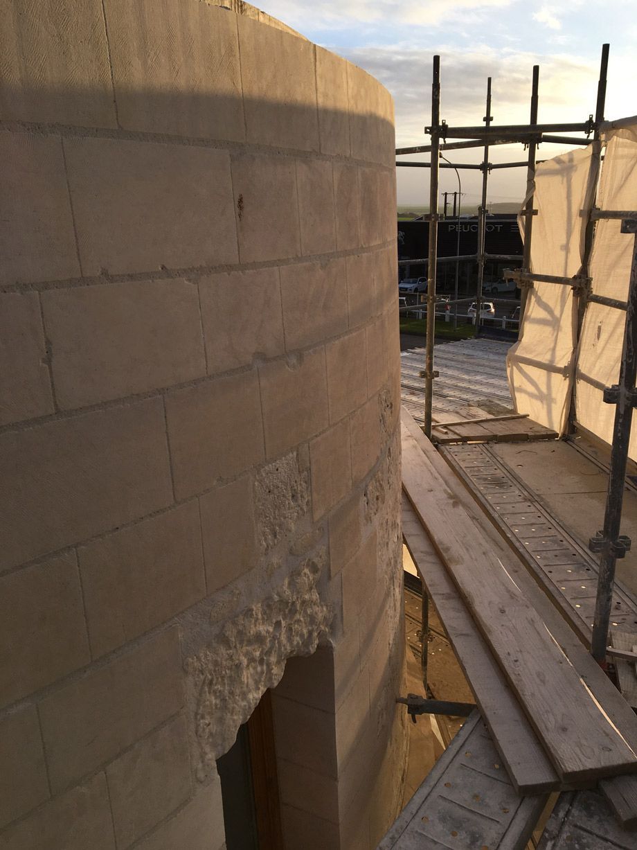 Construction extérieure d'un mur incurvé en briques claires avec un échafaudage et une passerelle en planches de bois.