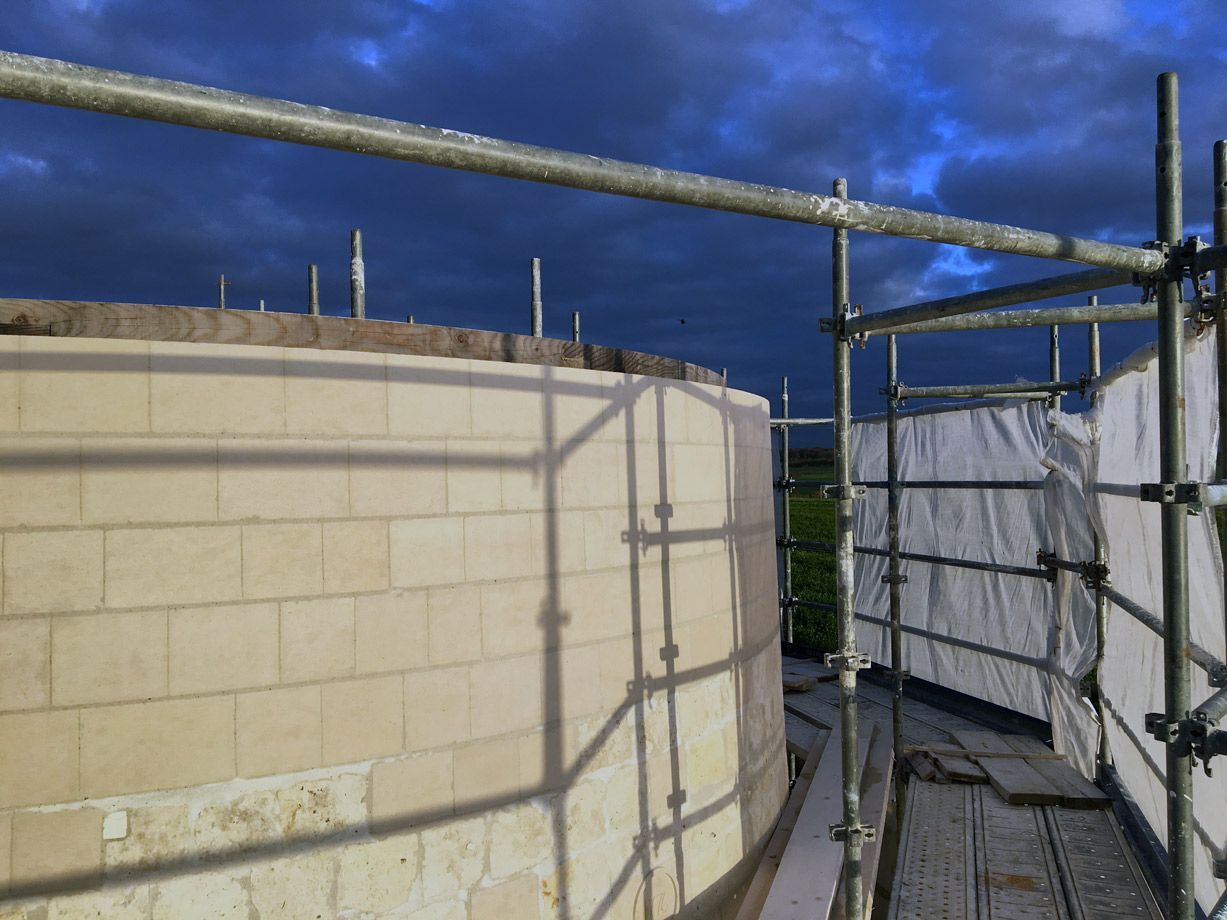 Des échafaudages de chantier entourent un bâtiment cylindrique sous un ciel nuageux.