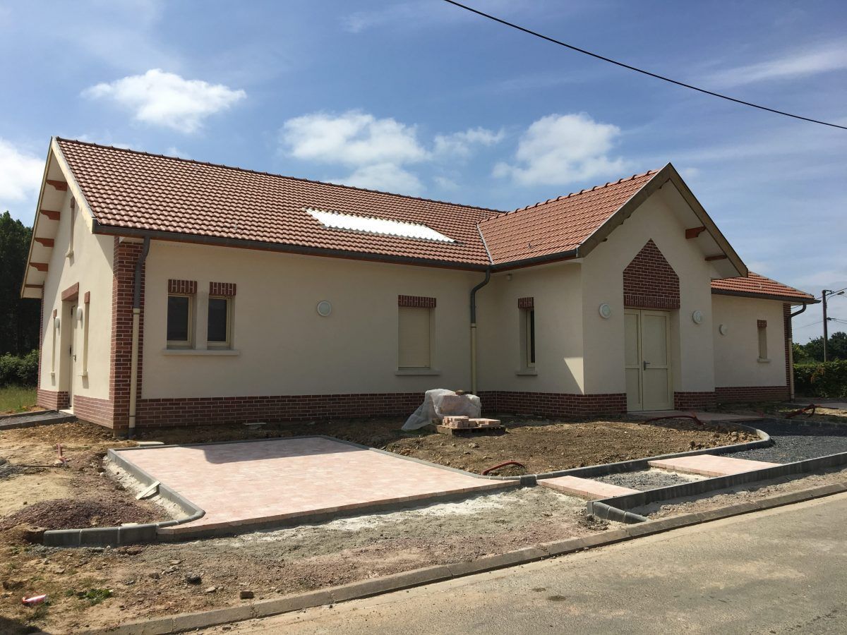 Maison neuve en construction avec toit de tuiles rouges, ornements en briques et murs beige clair.