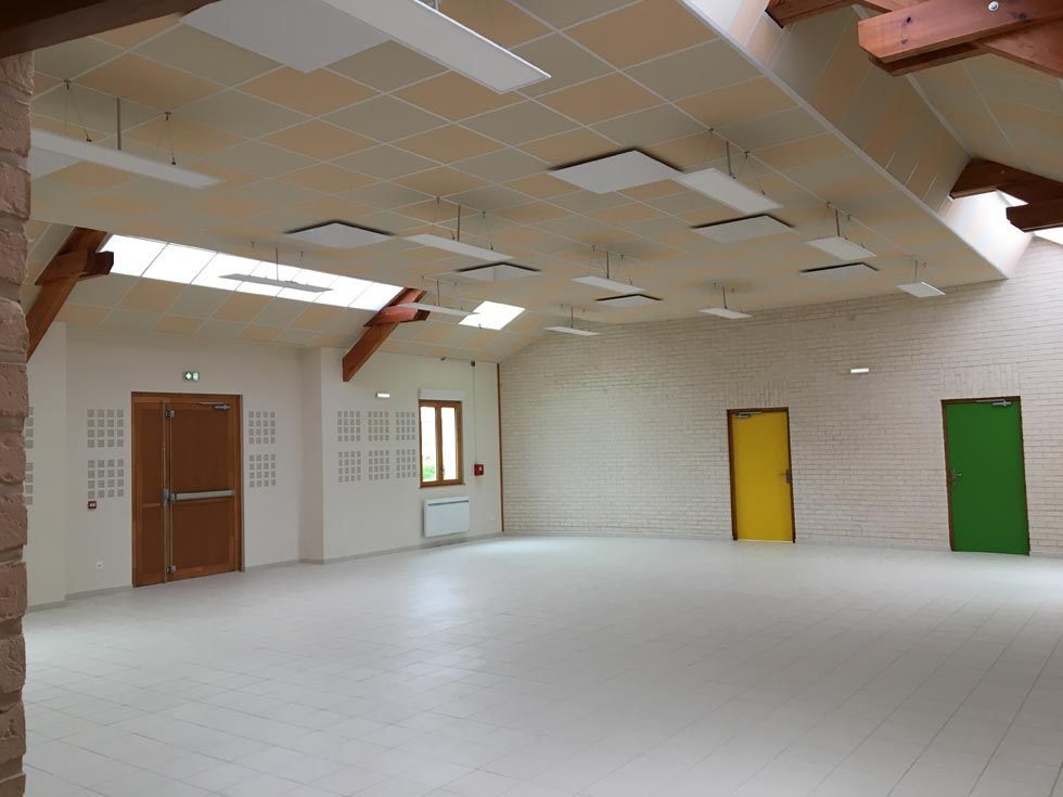 Hall vide et lumineux avec de multiples portes de couleurs variées, des fenêtres et des poutres en bois apparentes au plafond.