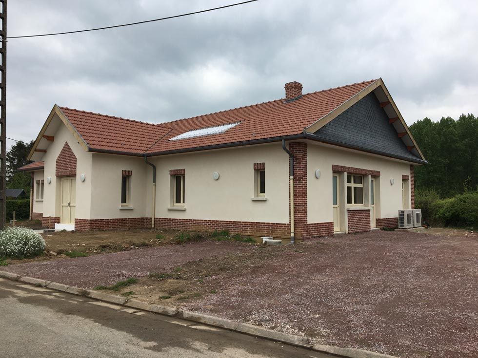 Un bâtiment couleur crème, avec un toit de tuiles en terre cuite et des accents de brique, se dresse sur une allée de gravier.