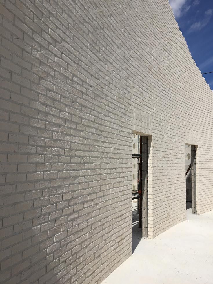 Mur de briques blanchies à la chaux avec deux portes ouvertes sous un ciel bleu.
