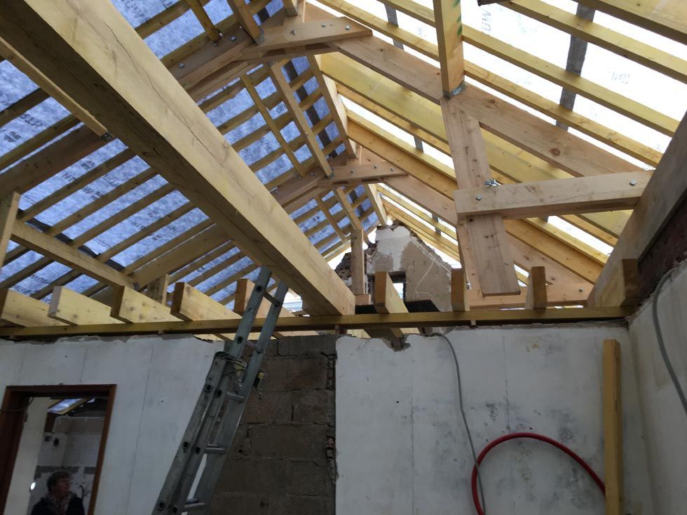 Vue intérieure d'un bâtiment en construction, montrant la charpente du toit en bois et une échelle.