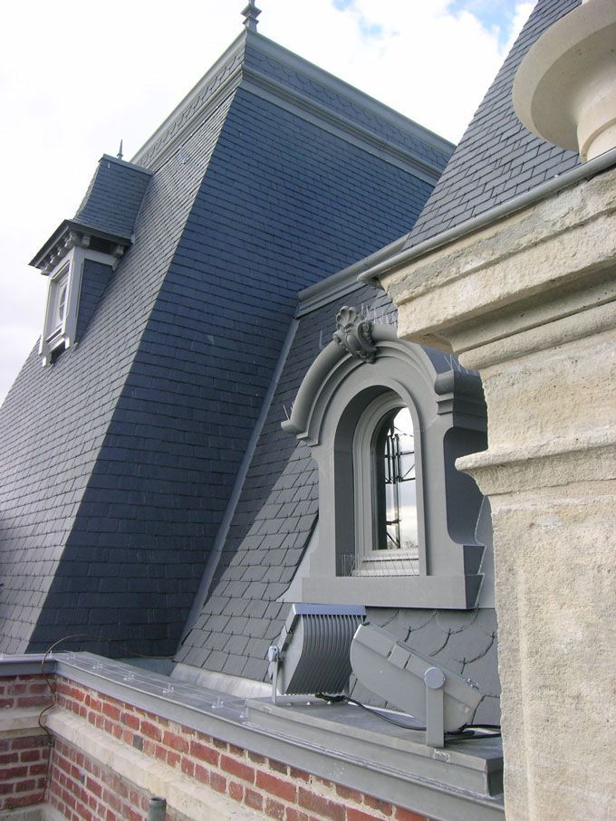 Toit en ardoise bleu foncé avec lucarne, ornements travaillés et mur en briques.