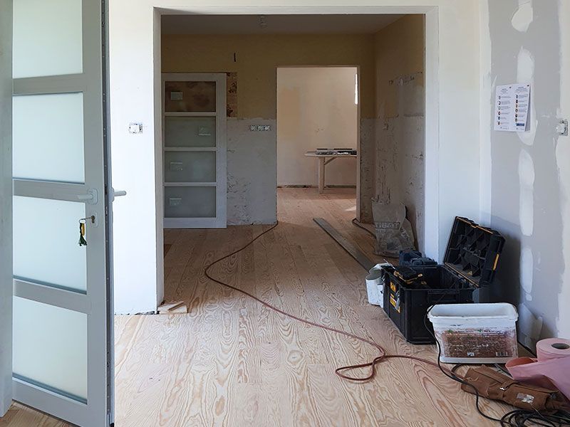 Rénovation intérieure avec parquet brut, portes ouvertes, outils et porte en verre dépoli.