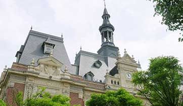 Bâtiment orné, doté d'une haute flèche et d'une tour d'horloge, présentant des détails en pierre et un toit en ardoise grise.