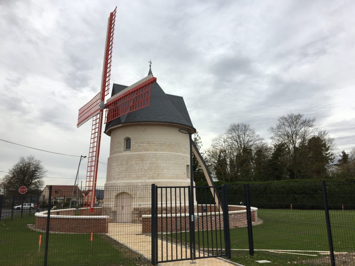 Moulin à vent aux pales rouges et à la base en briques, se détachant sur un ciel nuageux.