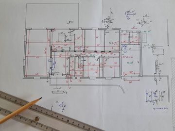 Plan d'étage avec mesures détaillées et symboles électriques, à l'aide d'une règle et d'un crayon.