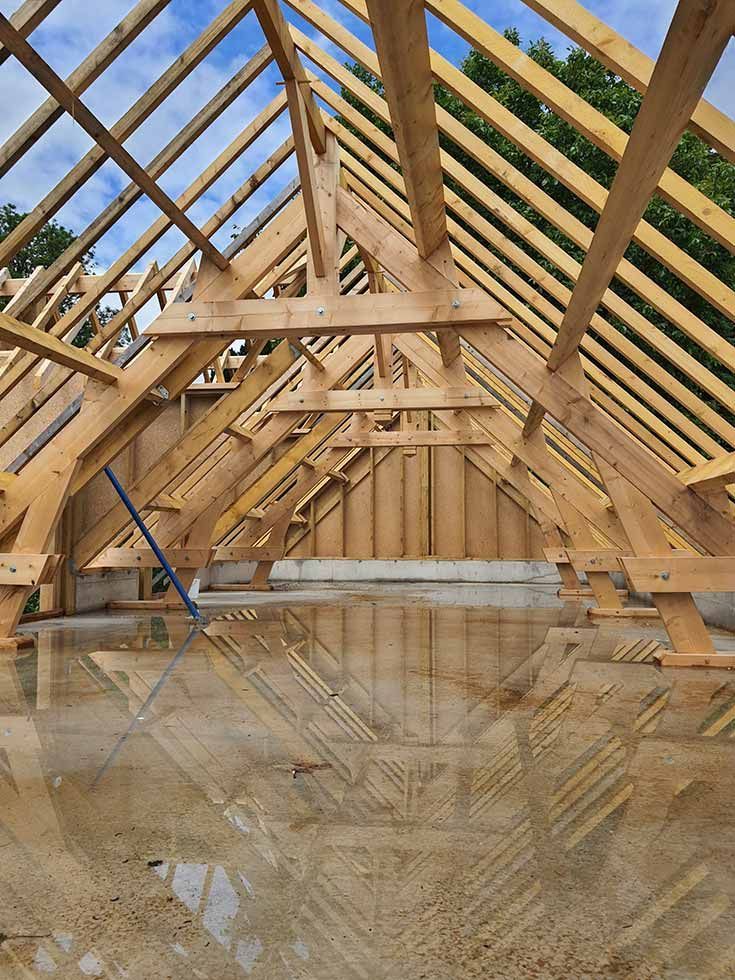 Charpente de toit en bois en construction, avec chevrons et poutres de soutien apparents. Ciel visible au-dessus.