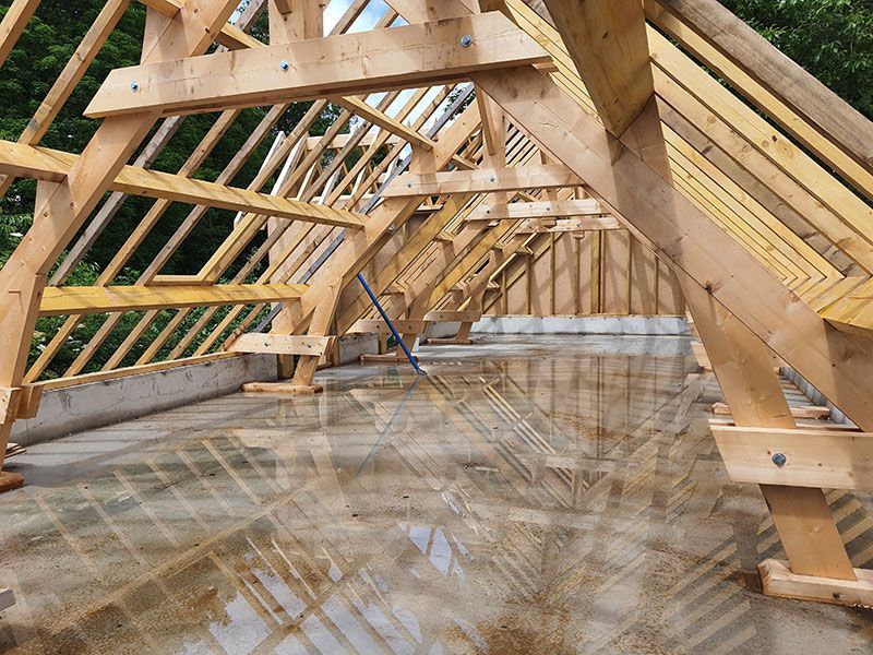 Charpente de toit en bois en construction ; poutres apparentes sur dalle de béton.