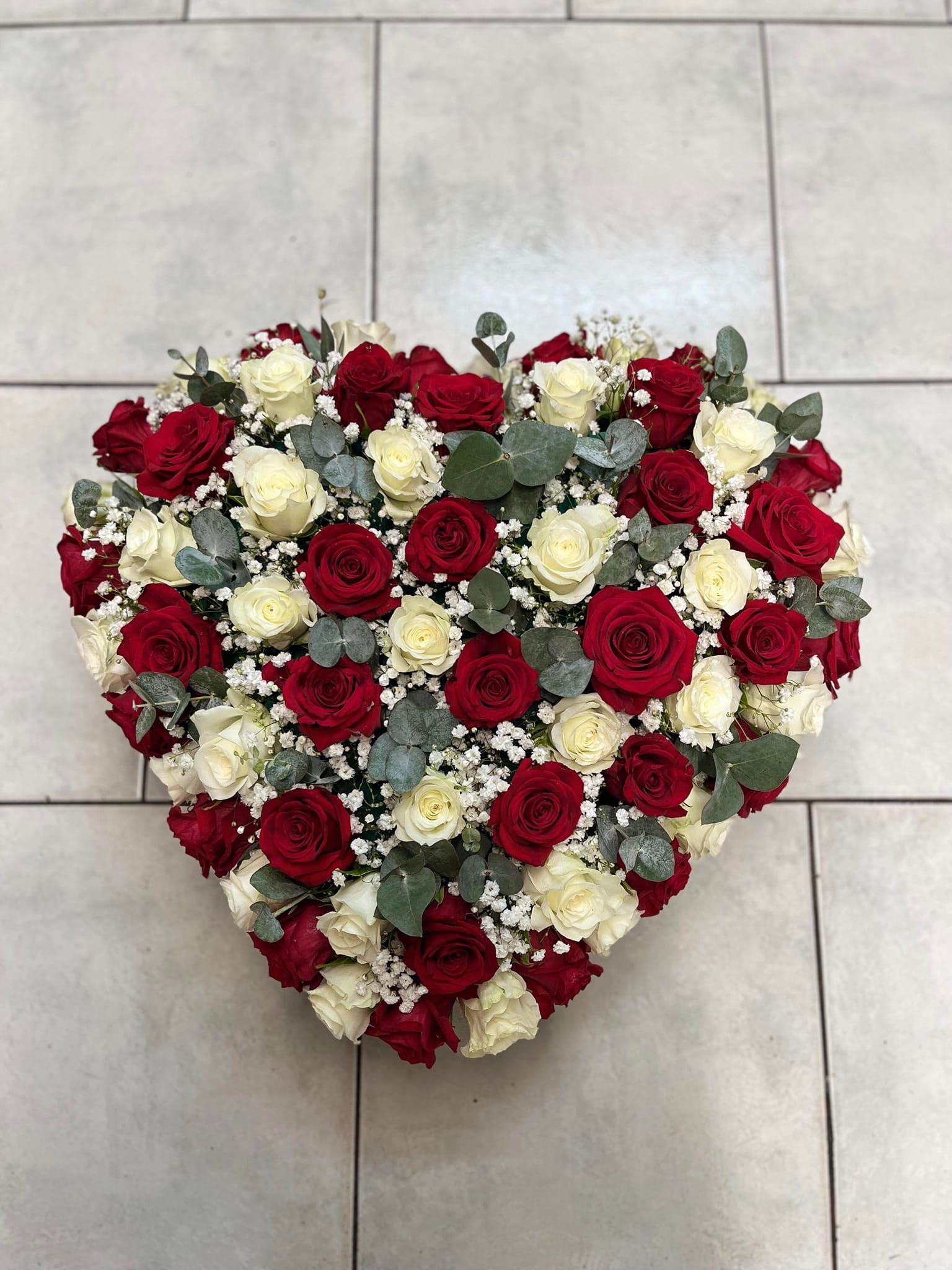 Composition en forme de cœur de roses rouges et blanches sur un sol carrelé