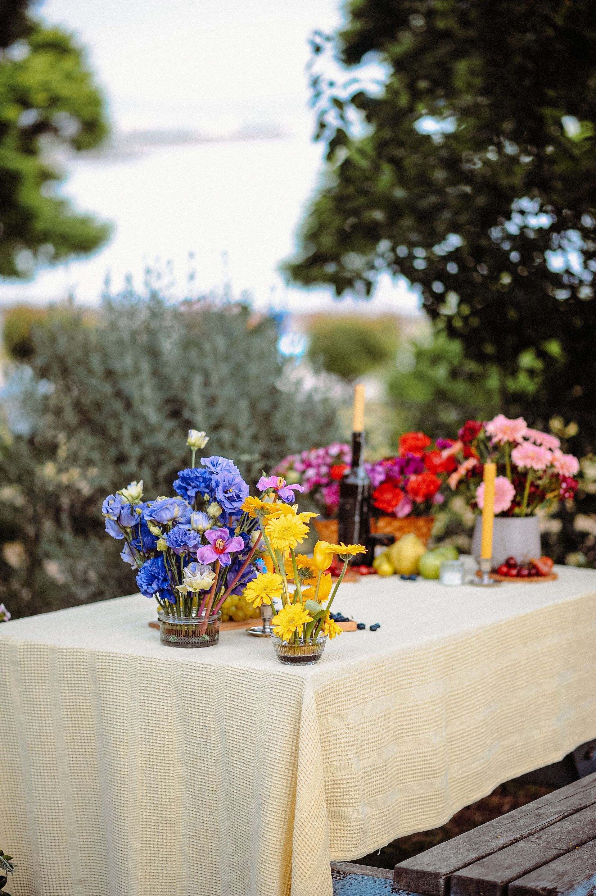 Table d'extérieur ornée de compositions florales colorées et de bougies sur une nappe couleur crème