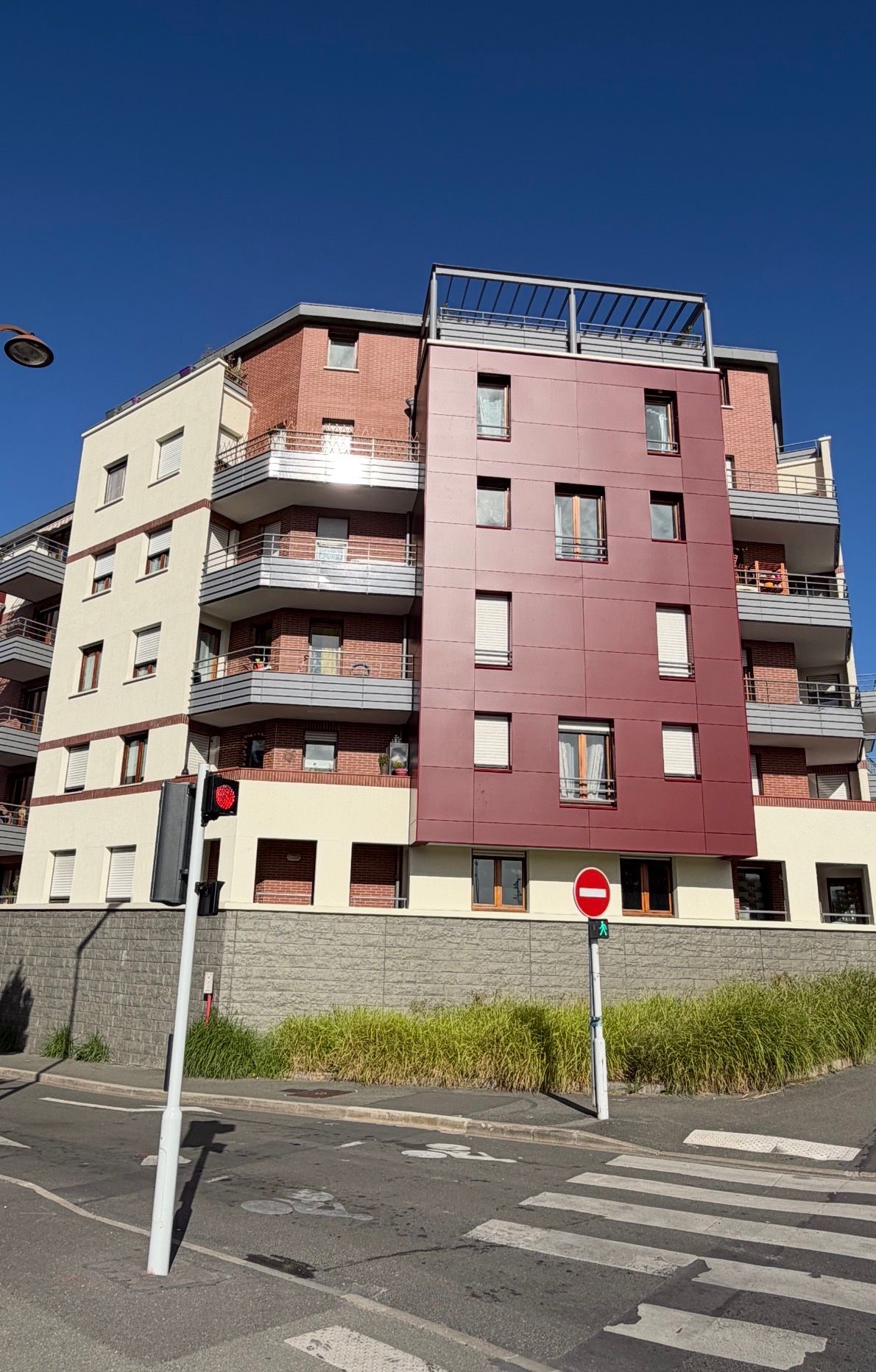Immeuble d'appartements moderne avec façade rouge, beige et brique sous un ciel bleu clair.