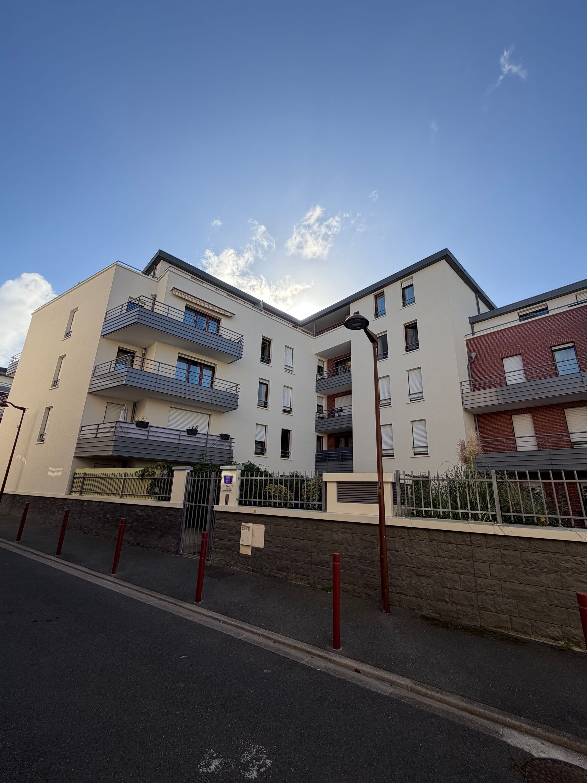 Immeuble d'appartements à plusieurs étages avec façade en briques blanches et rouges sous un ciel bleu avec soleil.
