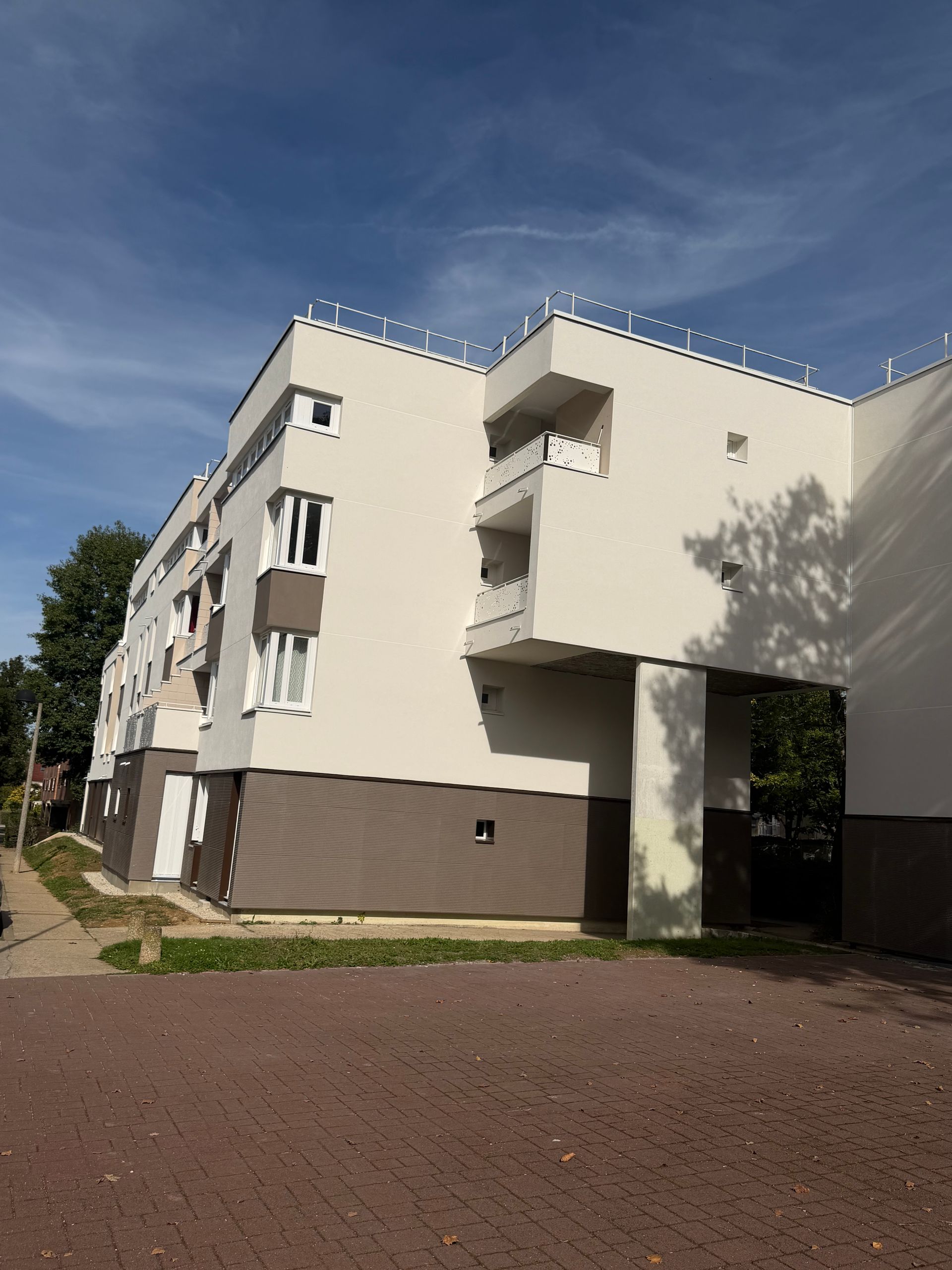 Immeuble d'appartements blanc et marron avec balcons, sous un ciel bleu.