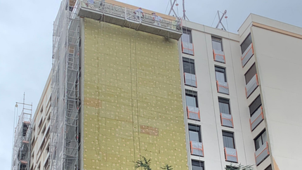 Extérieur du bâtiment en construction avec échafaudages et panneaux isolants.