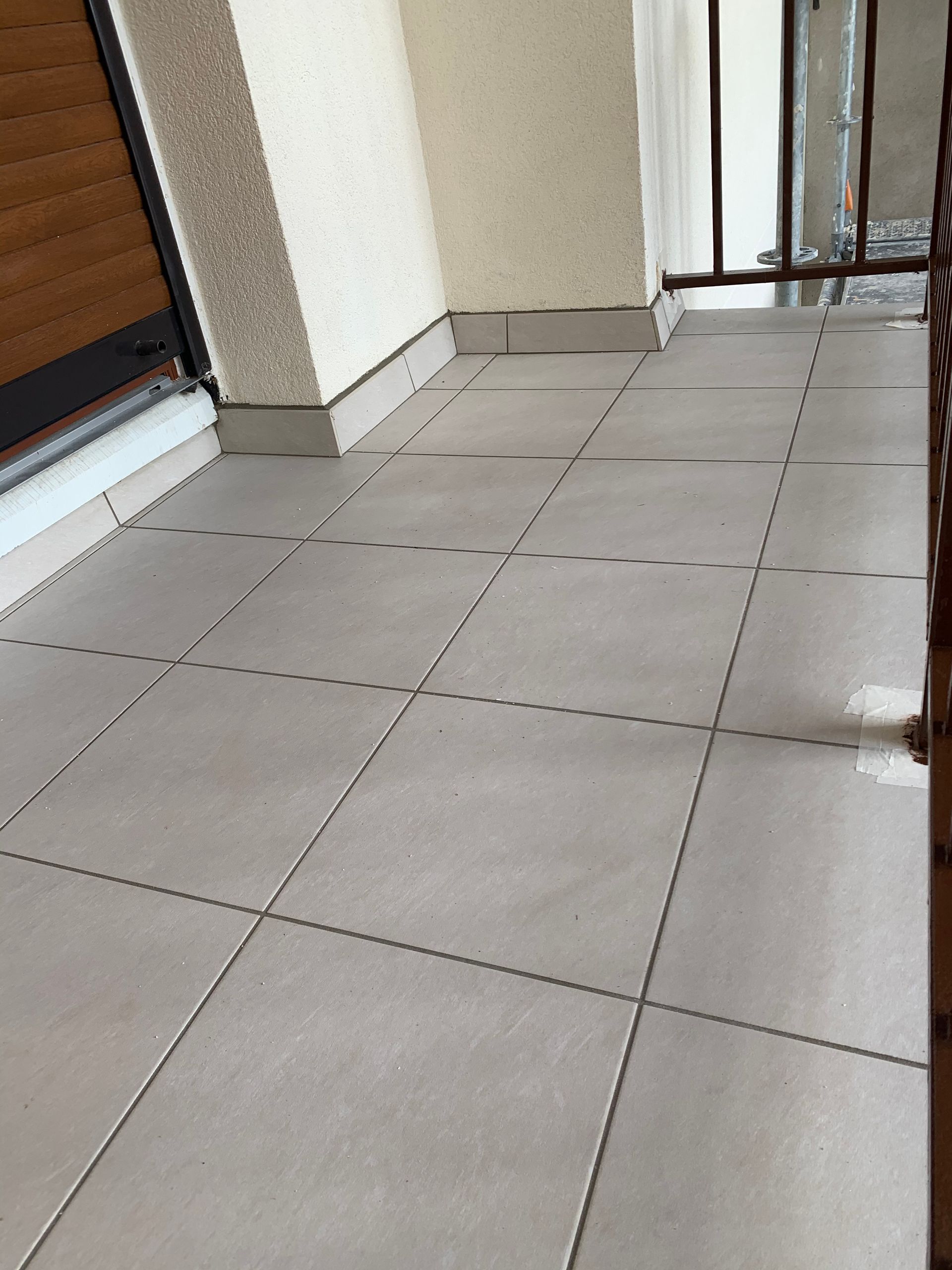 Balcon avec carrelage gris et murs blancs. Porte et garde-corps sur les côtés.