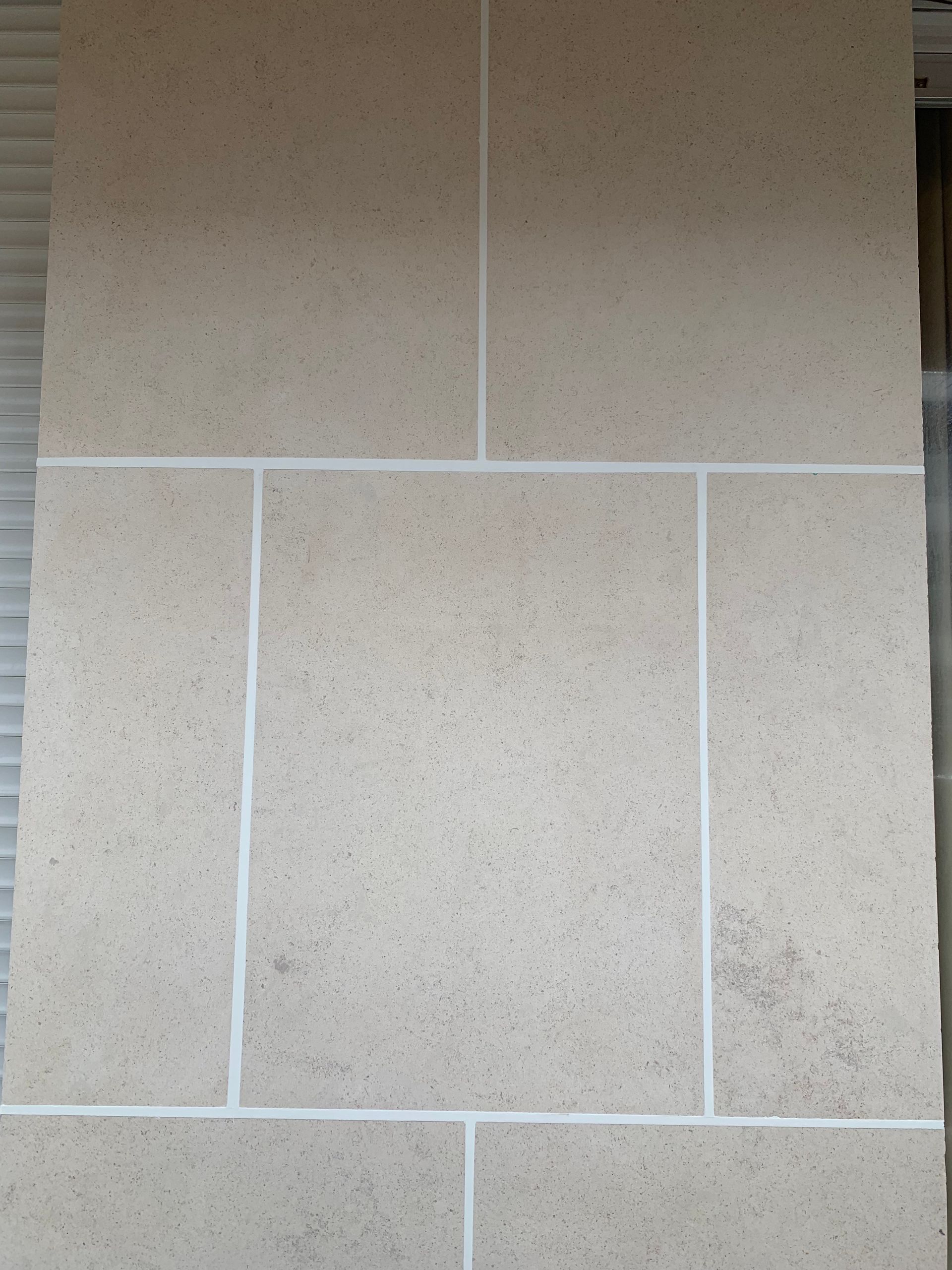 Mur en pierre beige avec joints blancs.