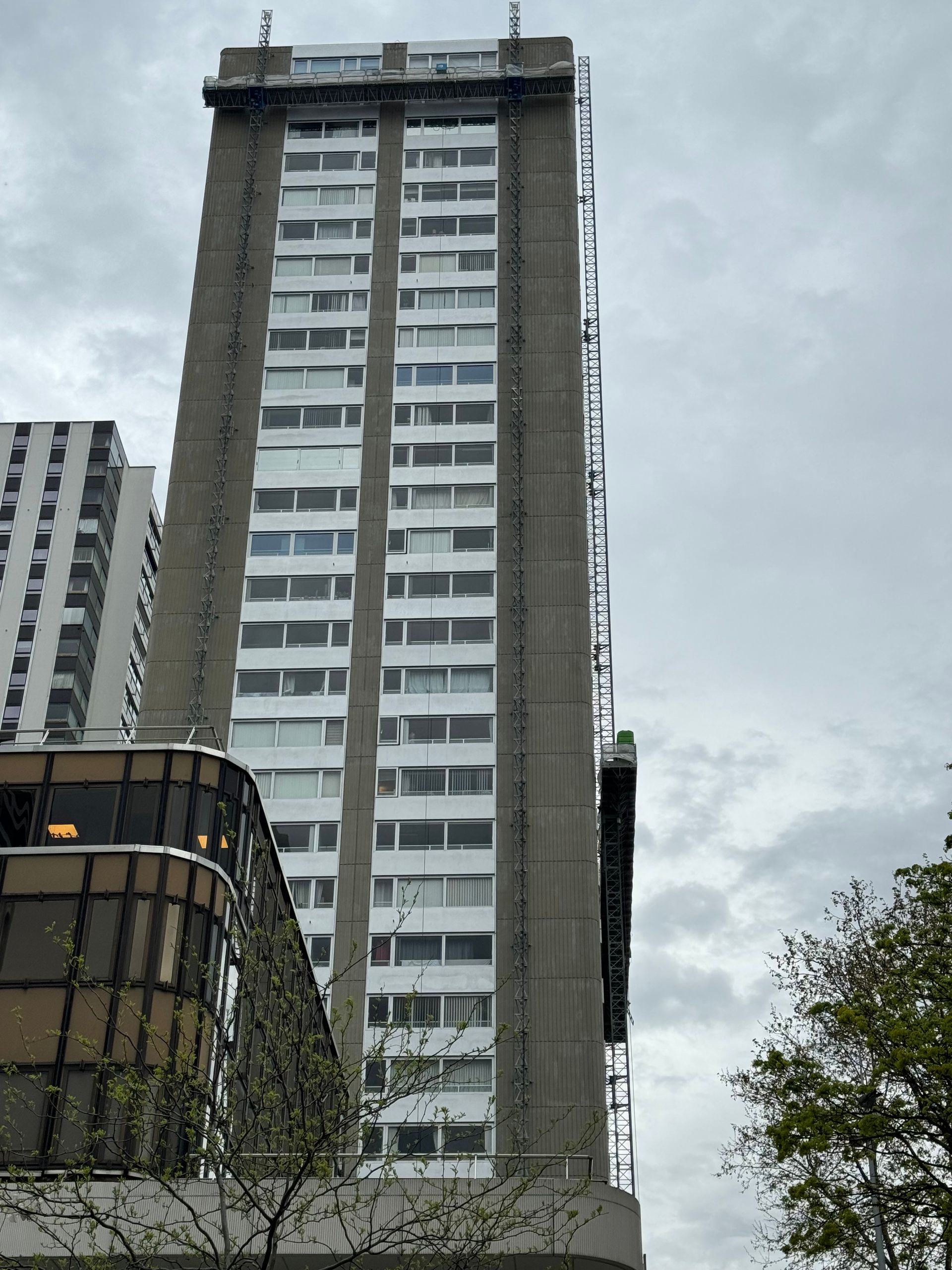 Grand immeuble d'appartements en béton avec de nombreuses fenêtres à cadre blanc, sur fond de ciel nuageux.