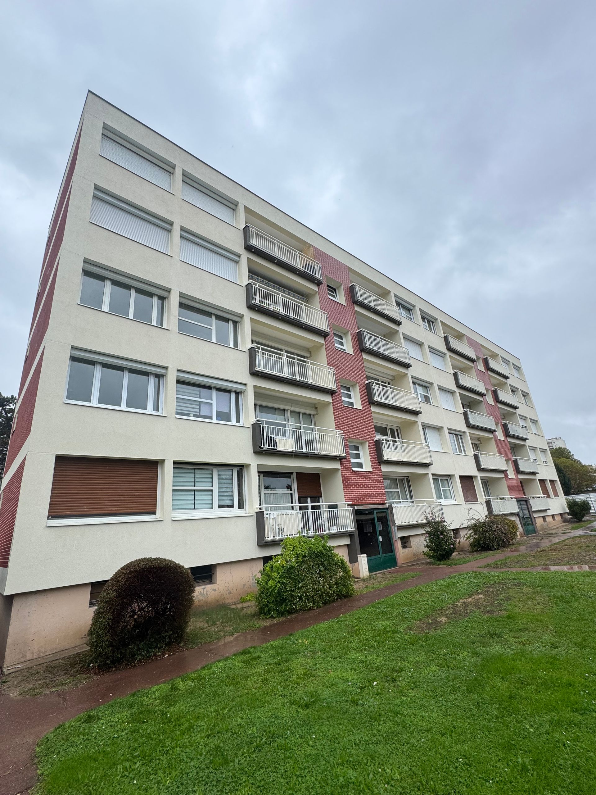 Immeuble d'appartements à plusieurs étages avec façade blanche et rouge, balcons et pelouse verte.