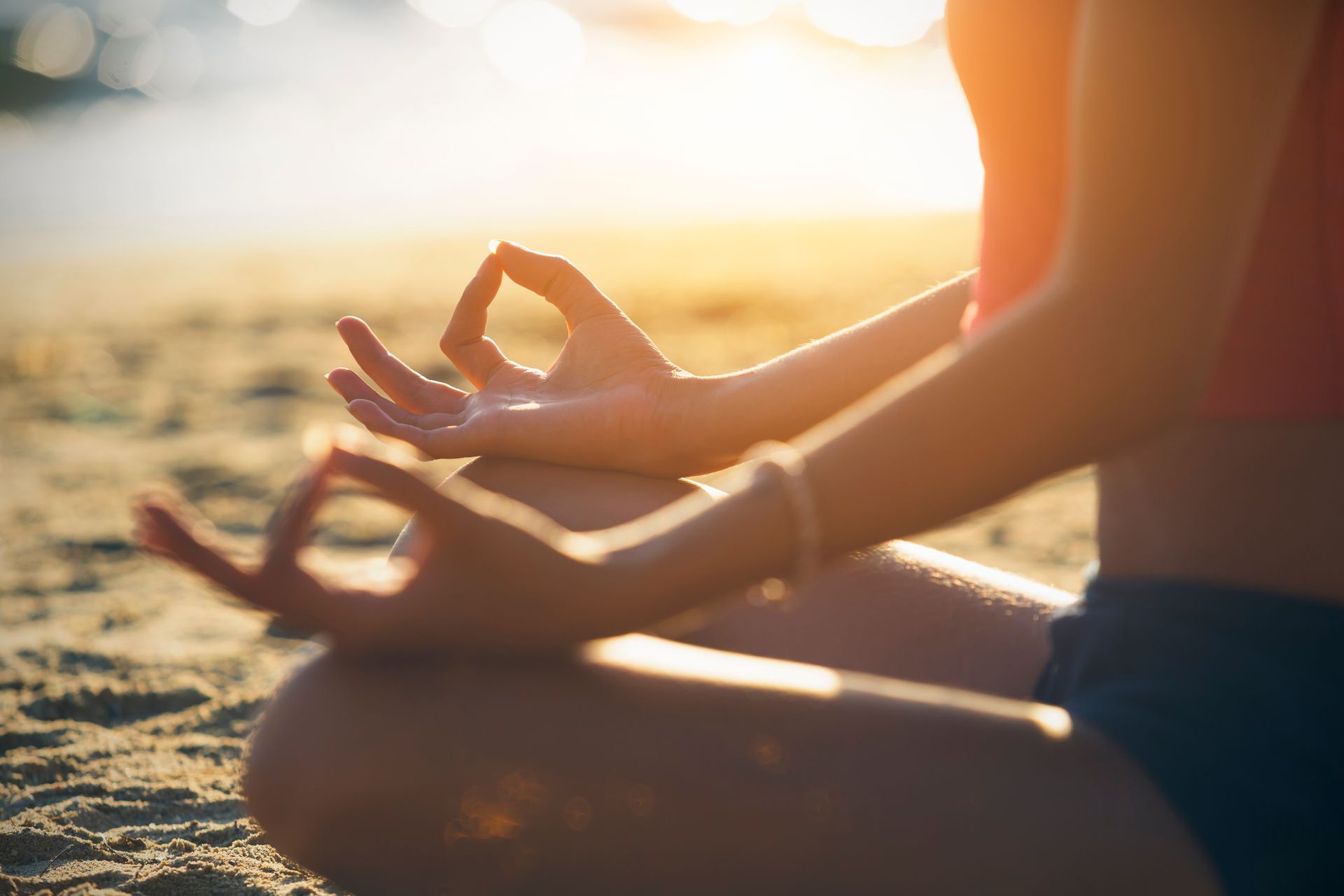 Personne en position du lotus sur une plage, les mains en mudra, avec la lumière du soleil.