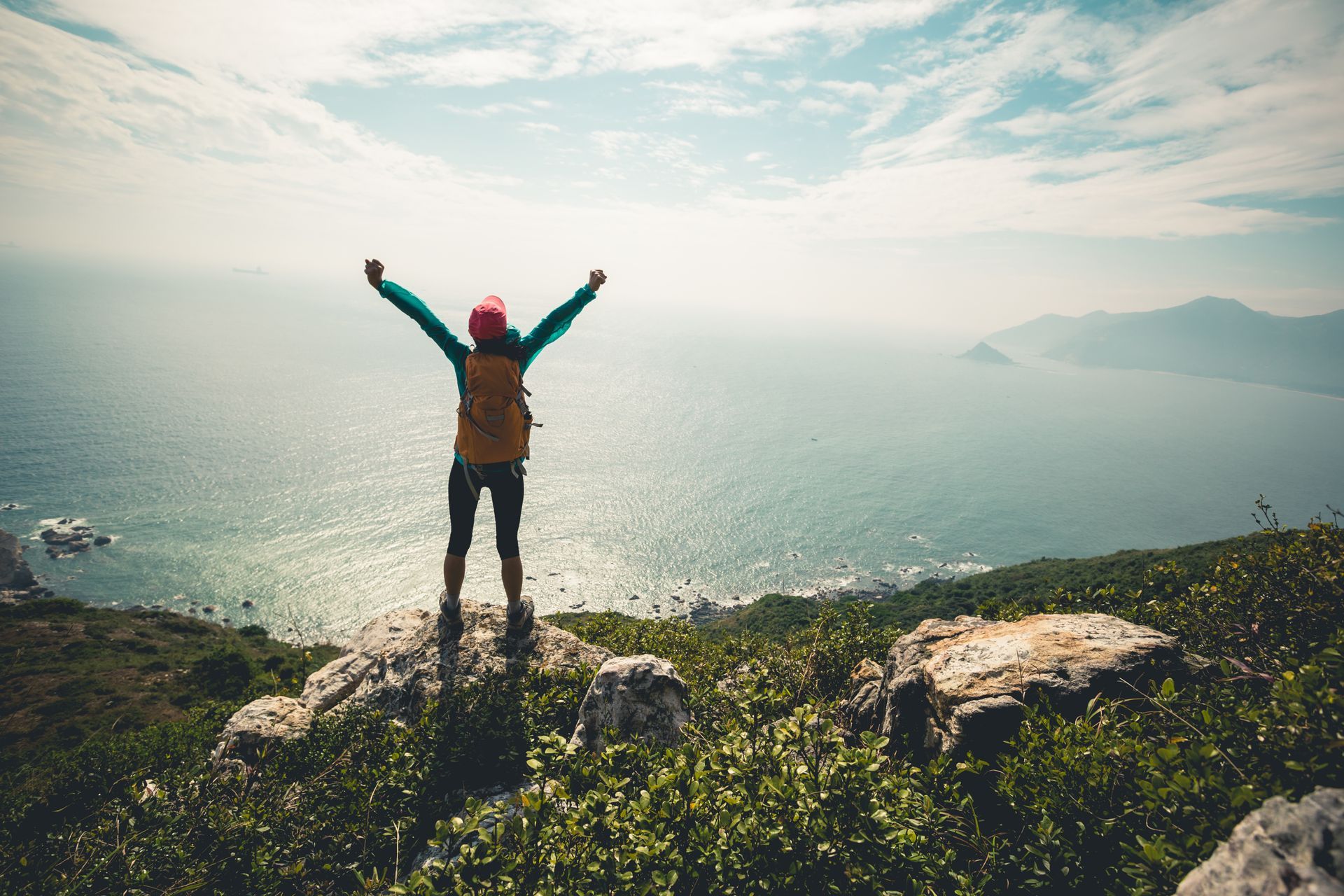 Personne avec les bras levés, debout au sommet d'une montagne surplombant l'océan.