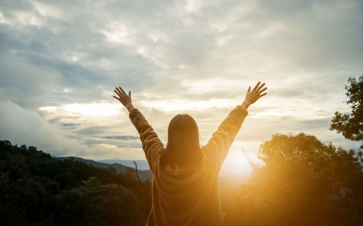 Femme aux bras levés, se découpant sur un ciel de coucher de soleil.