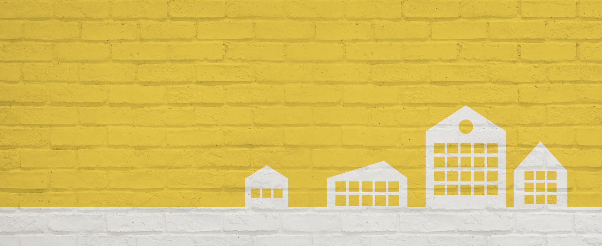 Silhouette blanche de maisons sur une base blanche, contre un mur de briques jaunes.