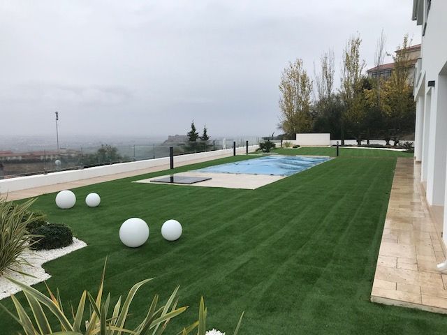 Un gran césped con una piscina al fondo.