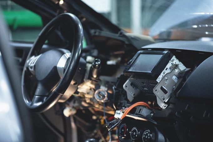 Dentro de un coche, un salpicadero dañado y cables expuestos junto al volante.