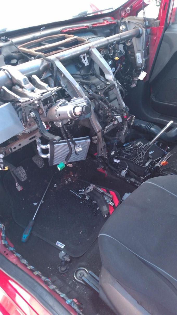 Interior del coche gravemente dañado con cableado del salpicadero expuesto y componentes despojados, asiento del pasajero delantero visible