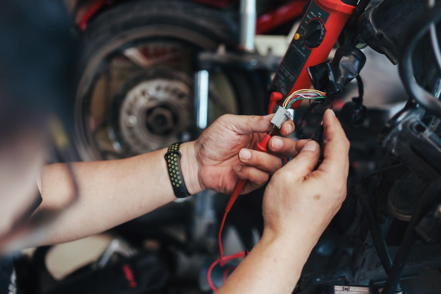 Manos reparando el motor de una motocicleta con cables rojos y negros en un taller.
