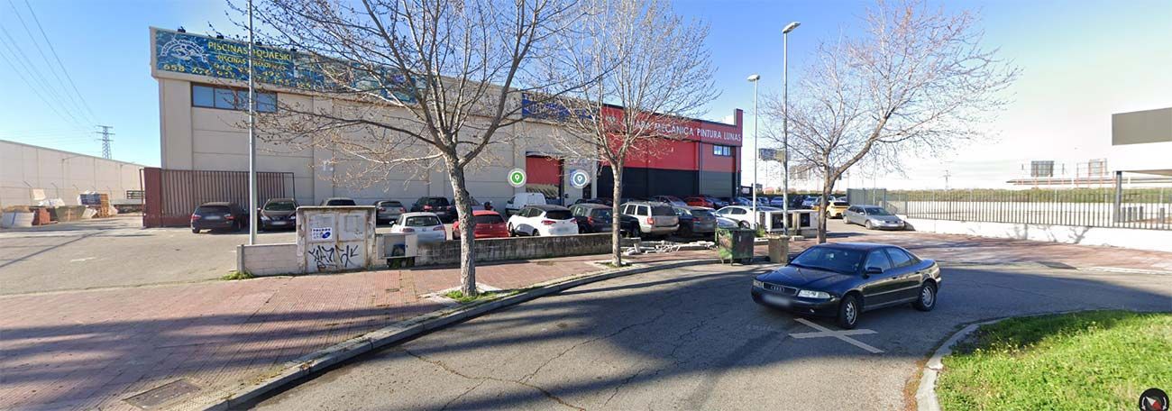 Furgoneta blanca y coche negro en el taller de un mecánico; una estructura de dos pisos en la parte trasera.