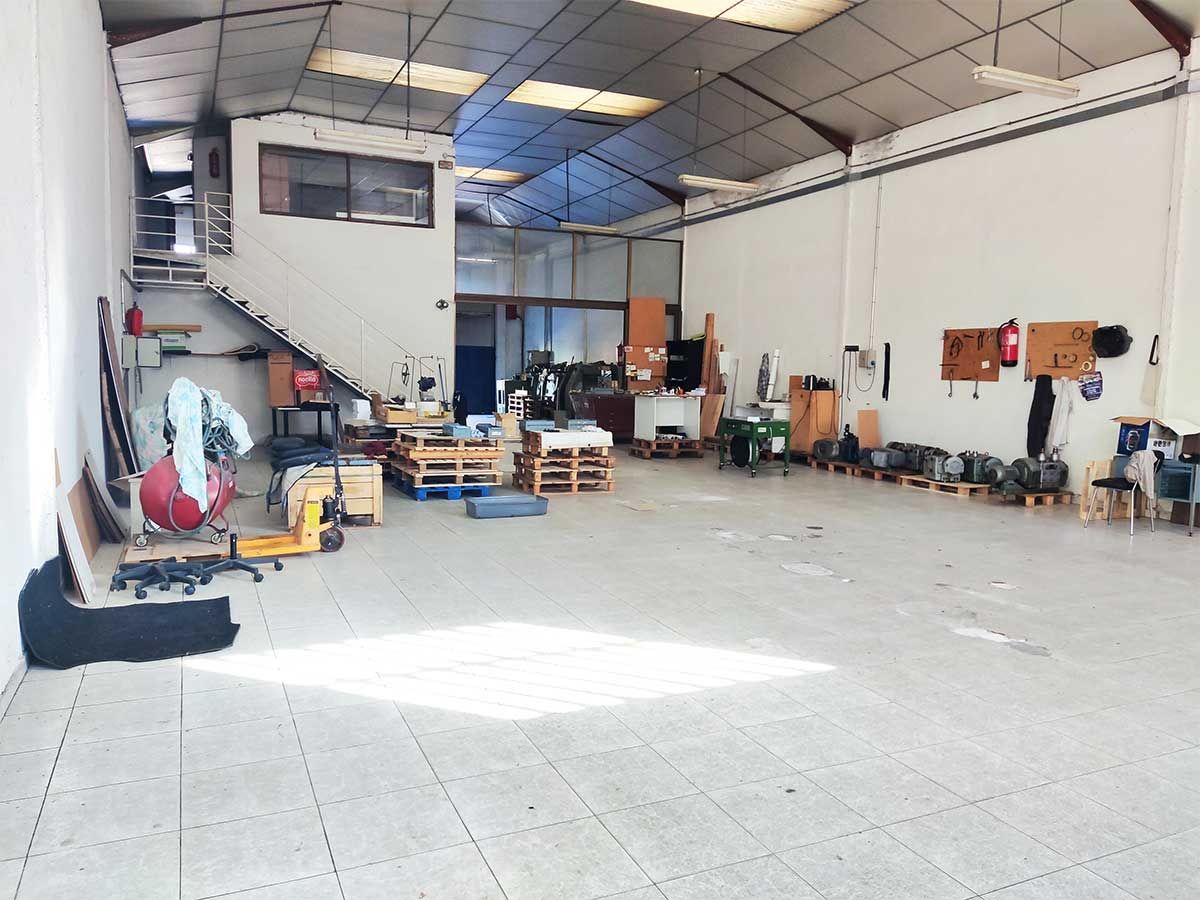 Gran interior de taller; paredes blancas, techo de metal, equipos y herramientas.