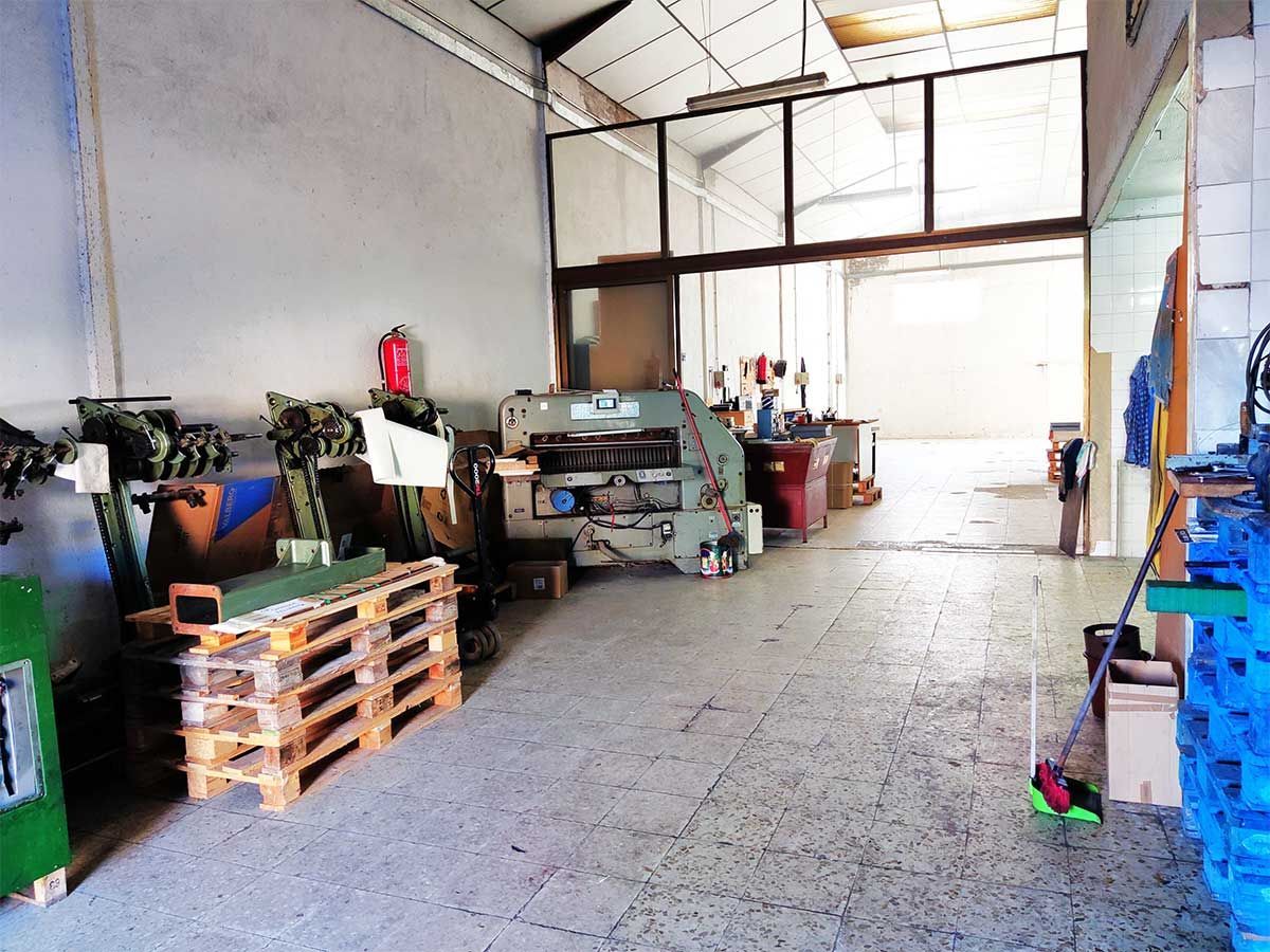 Gran interior de taller; paredes blancas, techo de metal, equipos y herramientas.