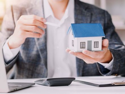 Persona sosteniendo una maqueta de casa y un papel, posiblemente para una operación inmobiliaria.