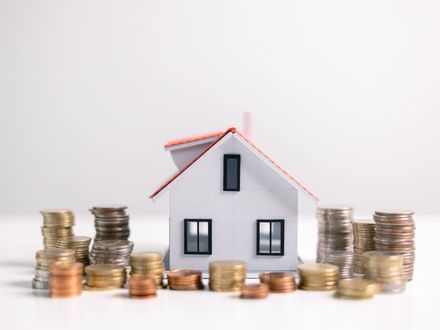 Casa de juguete blanca rodeada de pilas de monedas, que representa una inversión inmobiliaria.