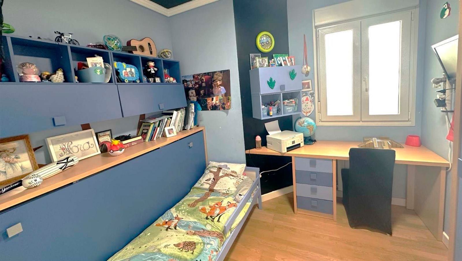 Un dormitorio con una cama, un escritorio, estanterías y una ventana.
