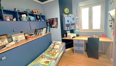 Dormitorio azul con cama, escritorio, estanterías y ventana.