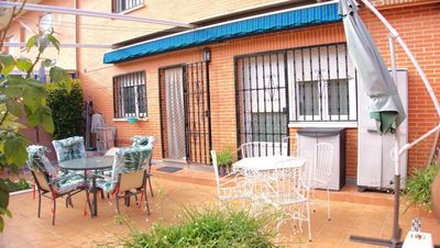 Patio exterior con mesa, sillas y toldo. Edificio de ladrillo, rejas de metal y sombrilla.