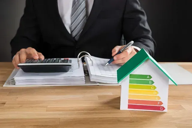 Persona de traje calculando finanzas junto a una casa modelo con etiqueta de clasificación de eficiencia energética.