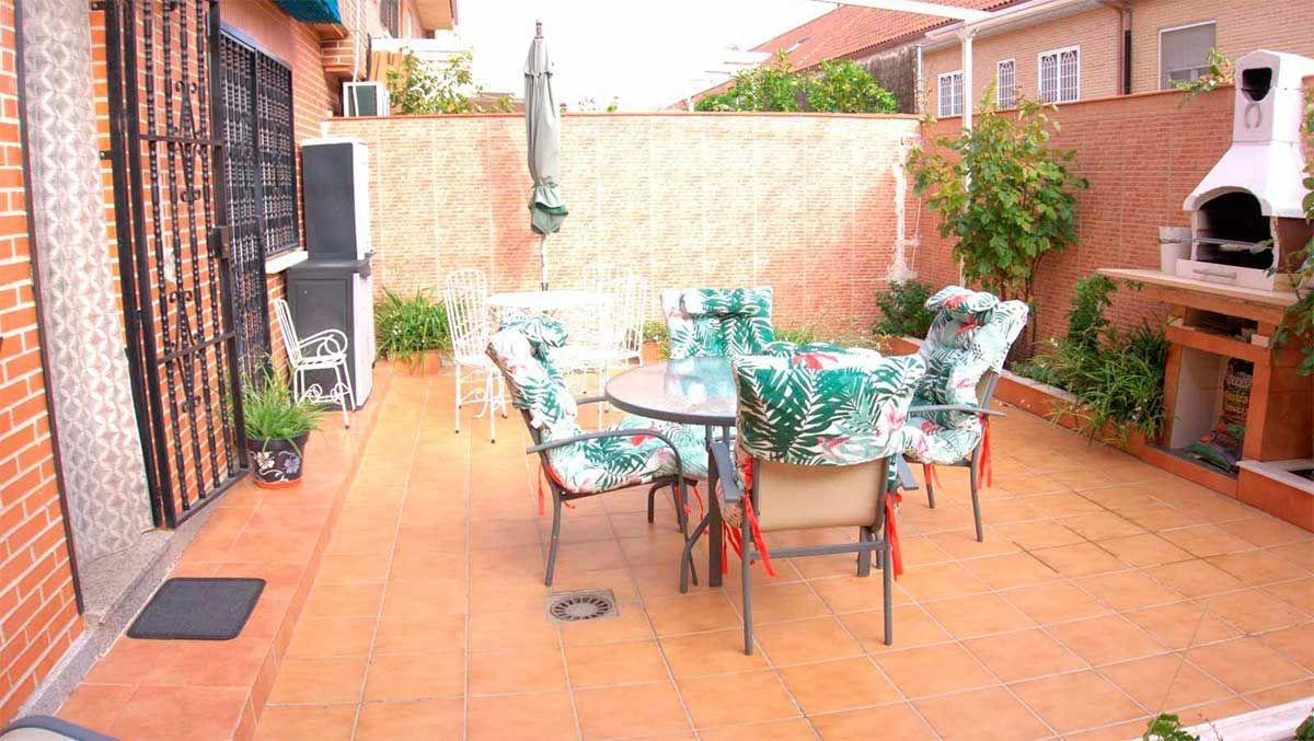 Edificio de ladrillo con patio; mesa, sillas, toldo y rejas de seguridad.