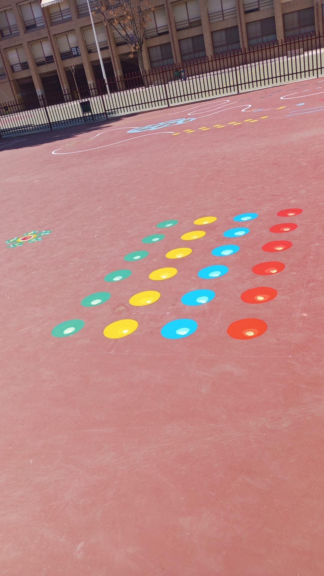 Conos circulares de colores dispuestos en filas sobre una cancha roja, con una valla al fondo.
