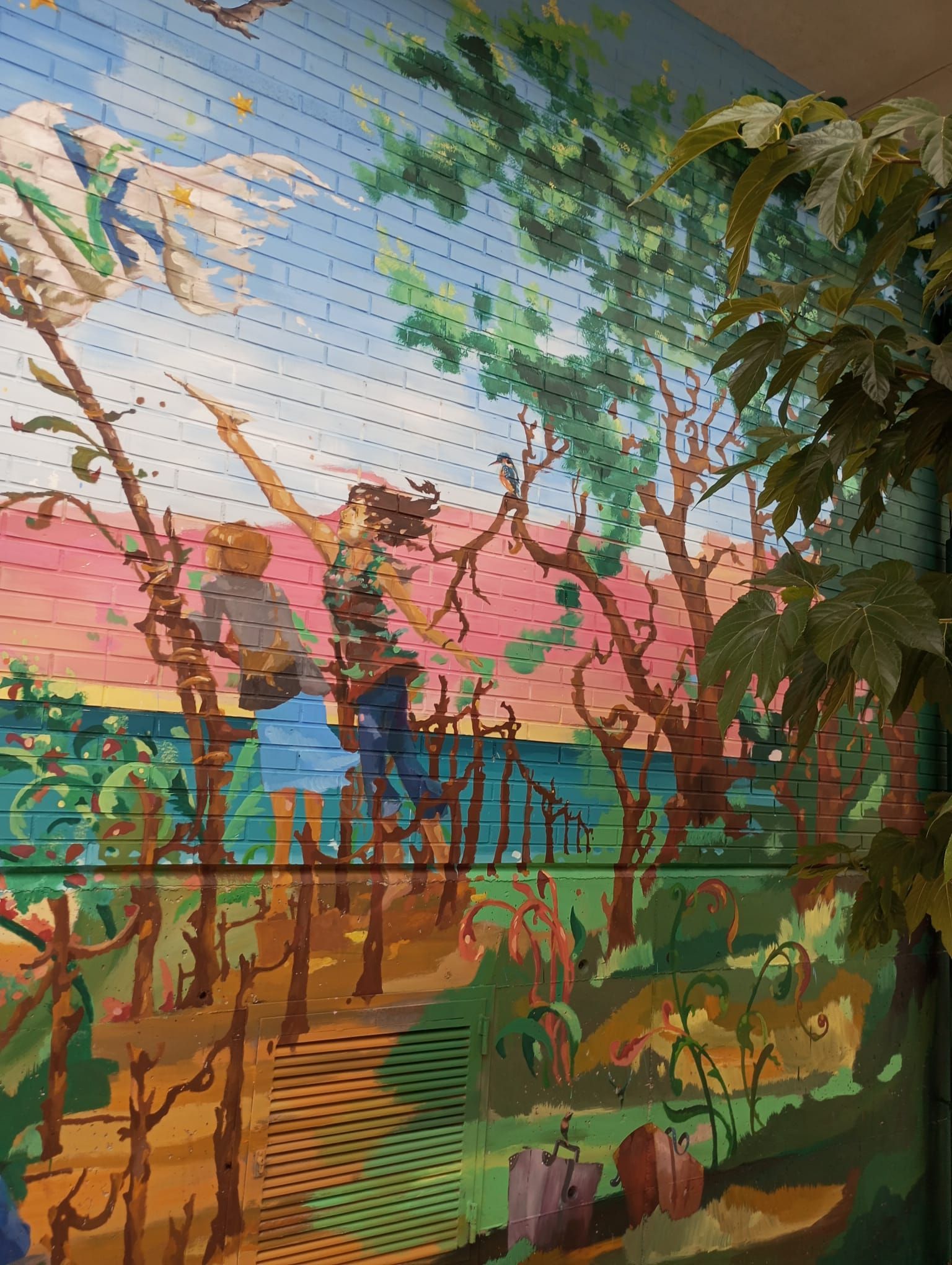 Mural colorido de árboles y pájaros tras un jardín frondoso al atardecer.