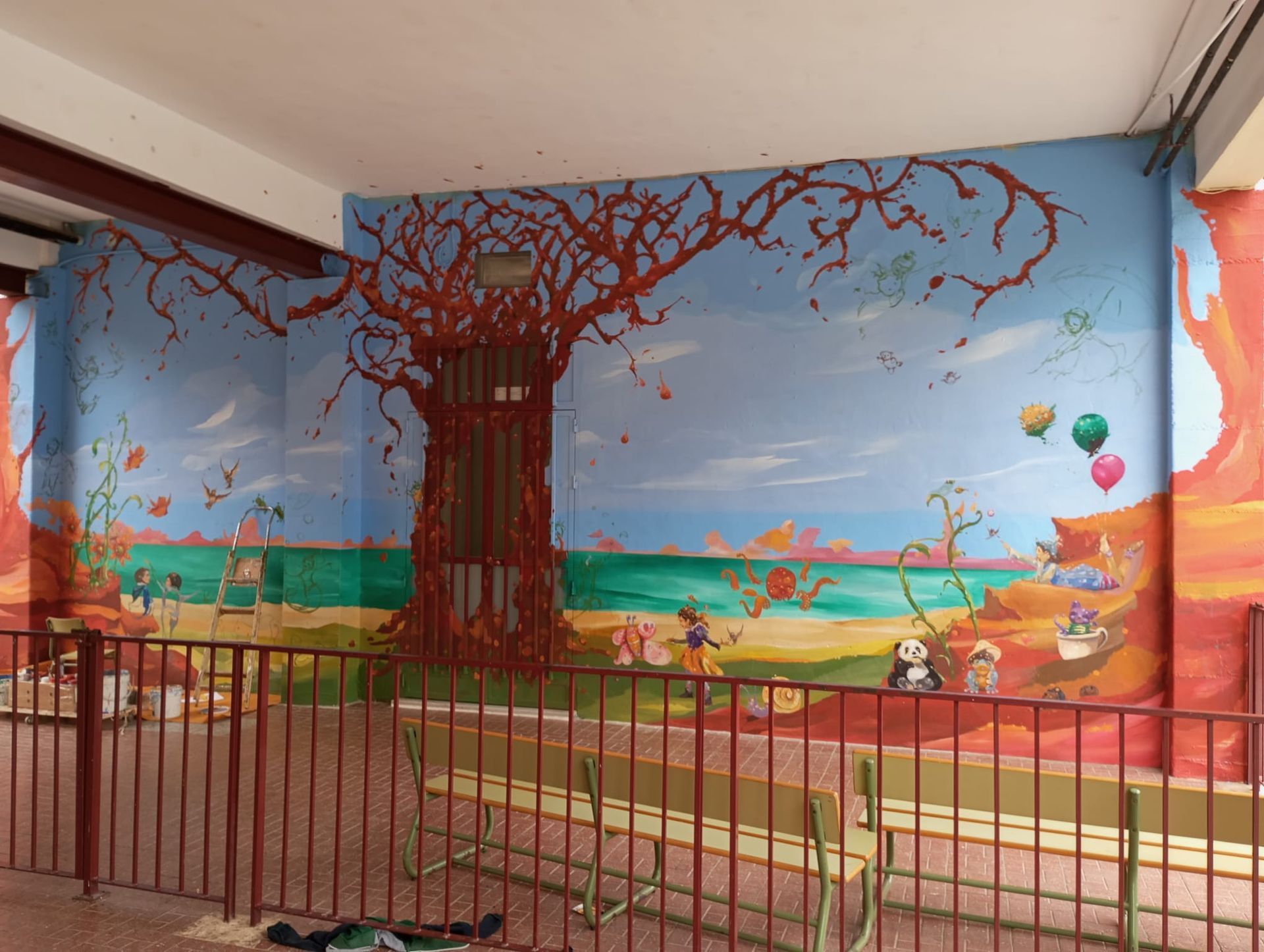 Mural colorido de un árbol y pájaros en una pared junto a una pasarela y rampa valladas.