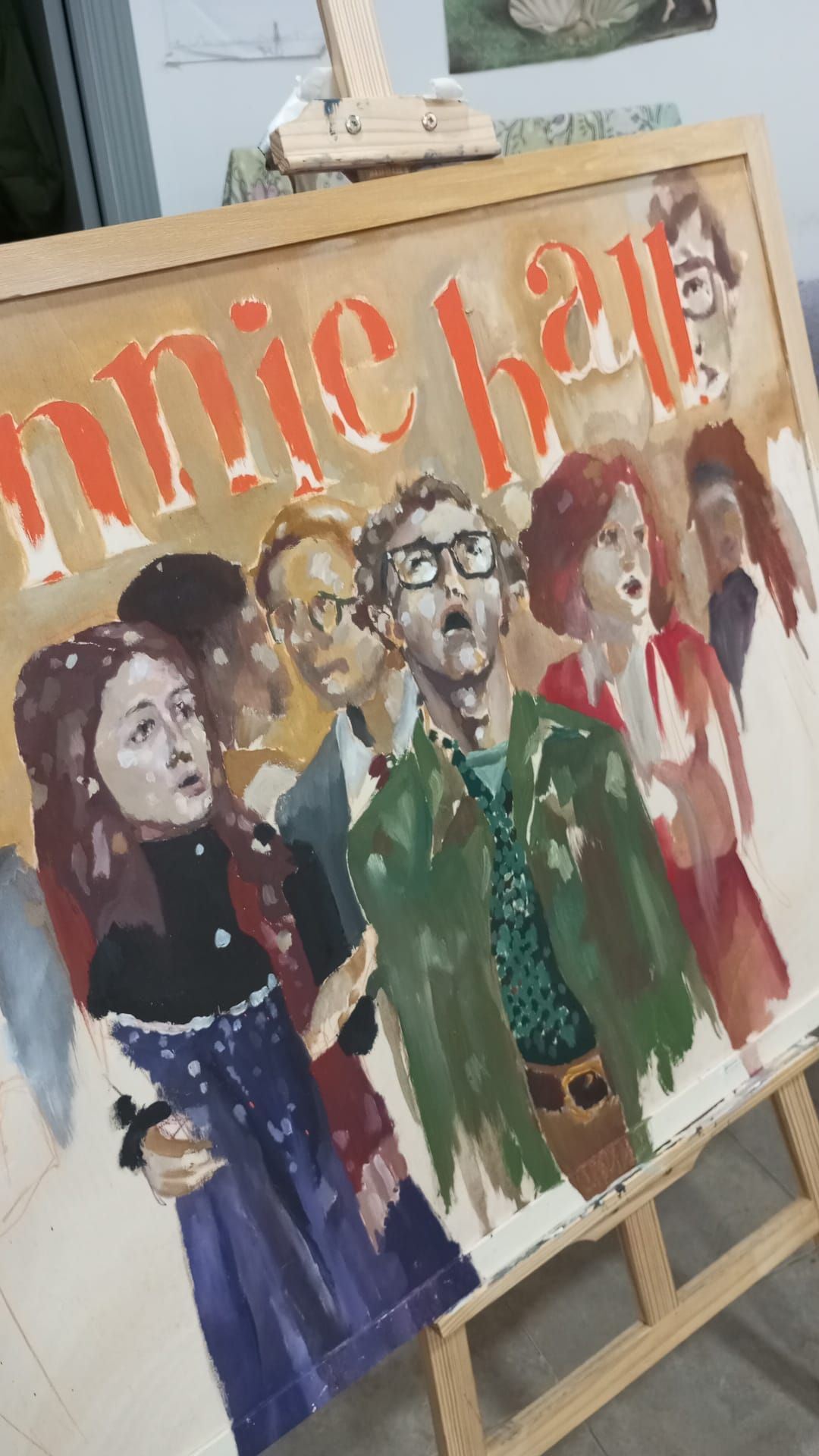 Pintura sobre caballete de cuatro figuras estilizadas con ropas coloridas junto a letras rojas parcialmente visibles.