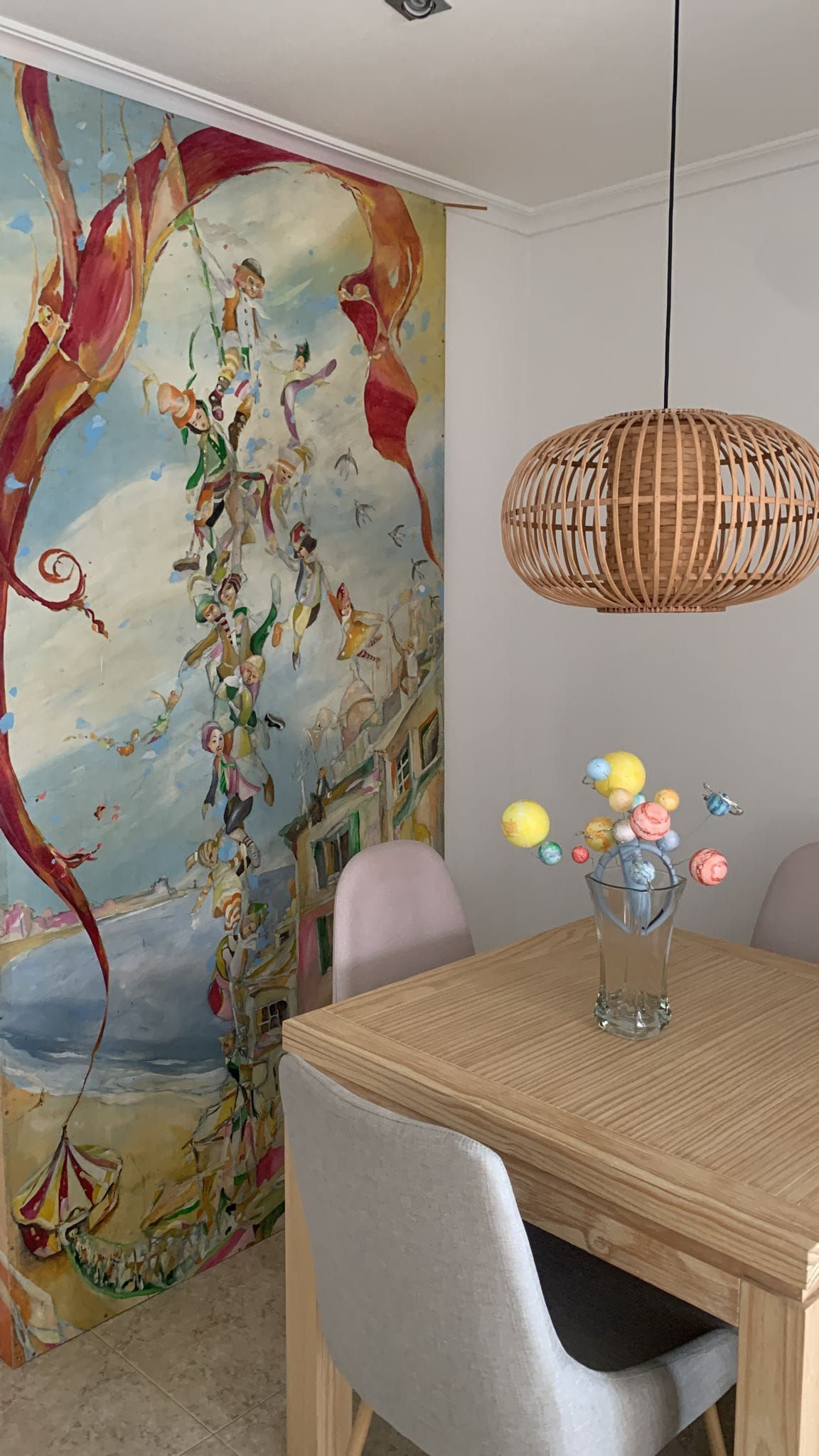 Acogedor rincón para comer con lámpara colgante tejida, mural floral en la pared y mesa de ratán decorada con flores.