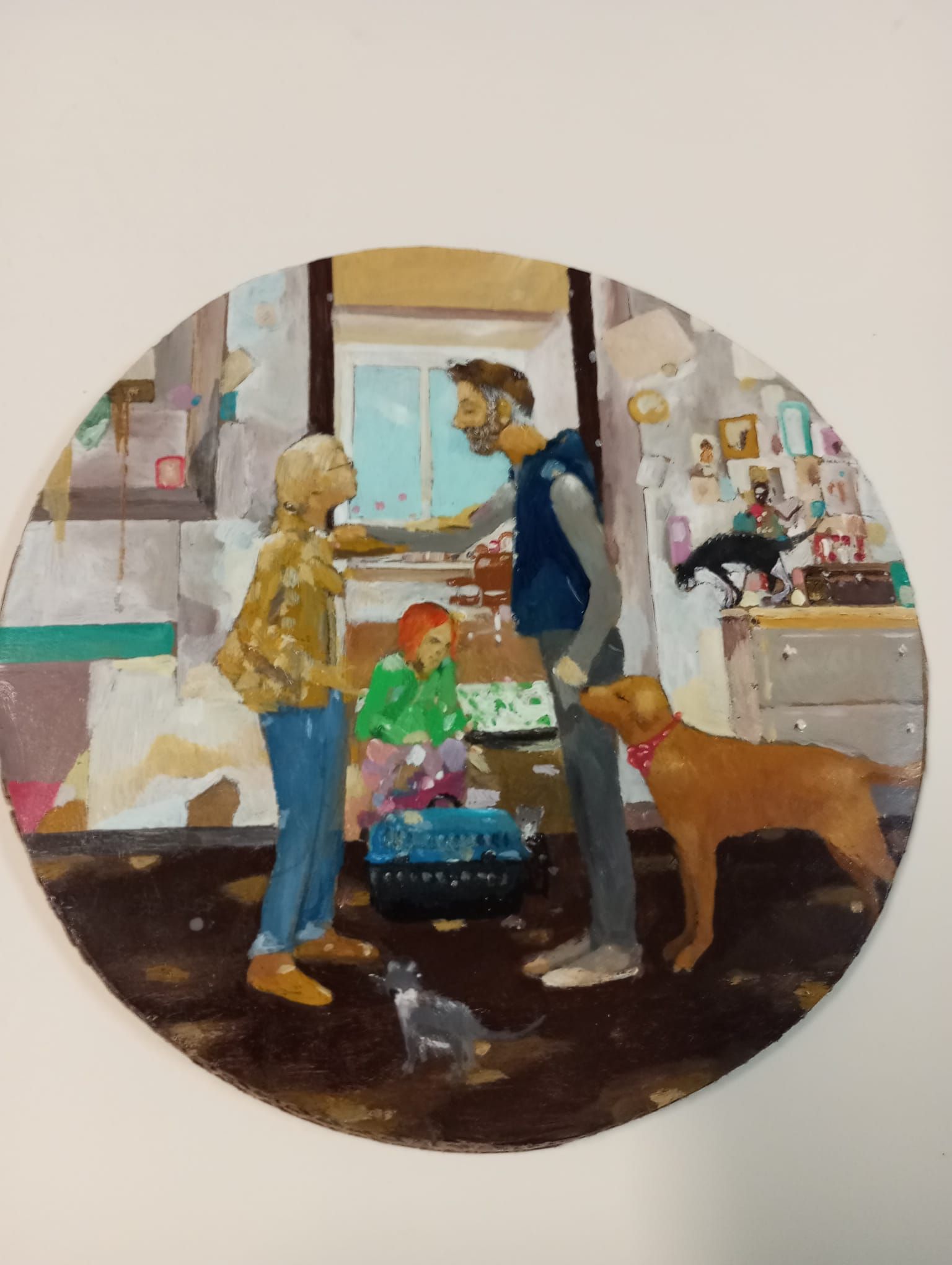Dos personas y un perro en un luminoso estudio de arte, con un niño sentado entre ellos cerca de unos cuadros.