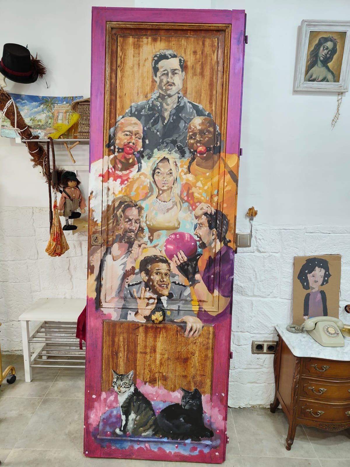 Panel alto de madera decorado con retratos pintados, en una habitación junto a obras de arte enmarcadas y una mesita.